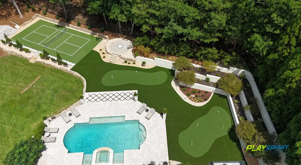 Aerial view of an estate backyard with a pickleball court, putting greens and a pool