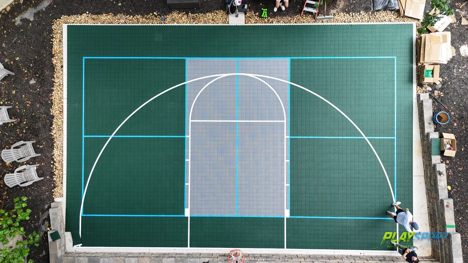Aerial view of a green PlaySport modular basketball court with cyan game lines and a grey key during tile installation