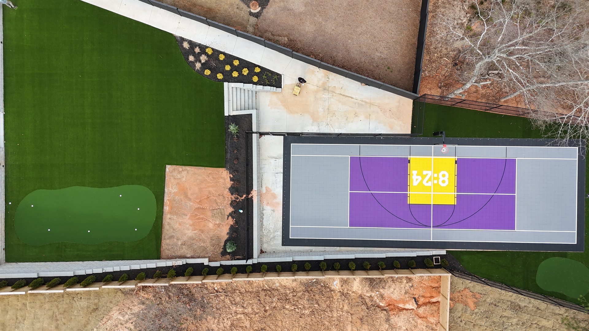Finished backyard basketball court with purple and grey tiles, a Kobe 8:24 tribute key, putting green and turf lawn — PlaySport Courts