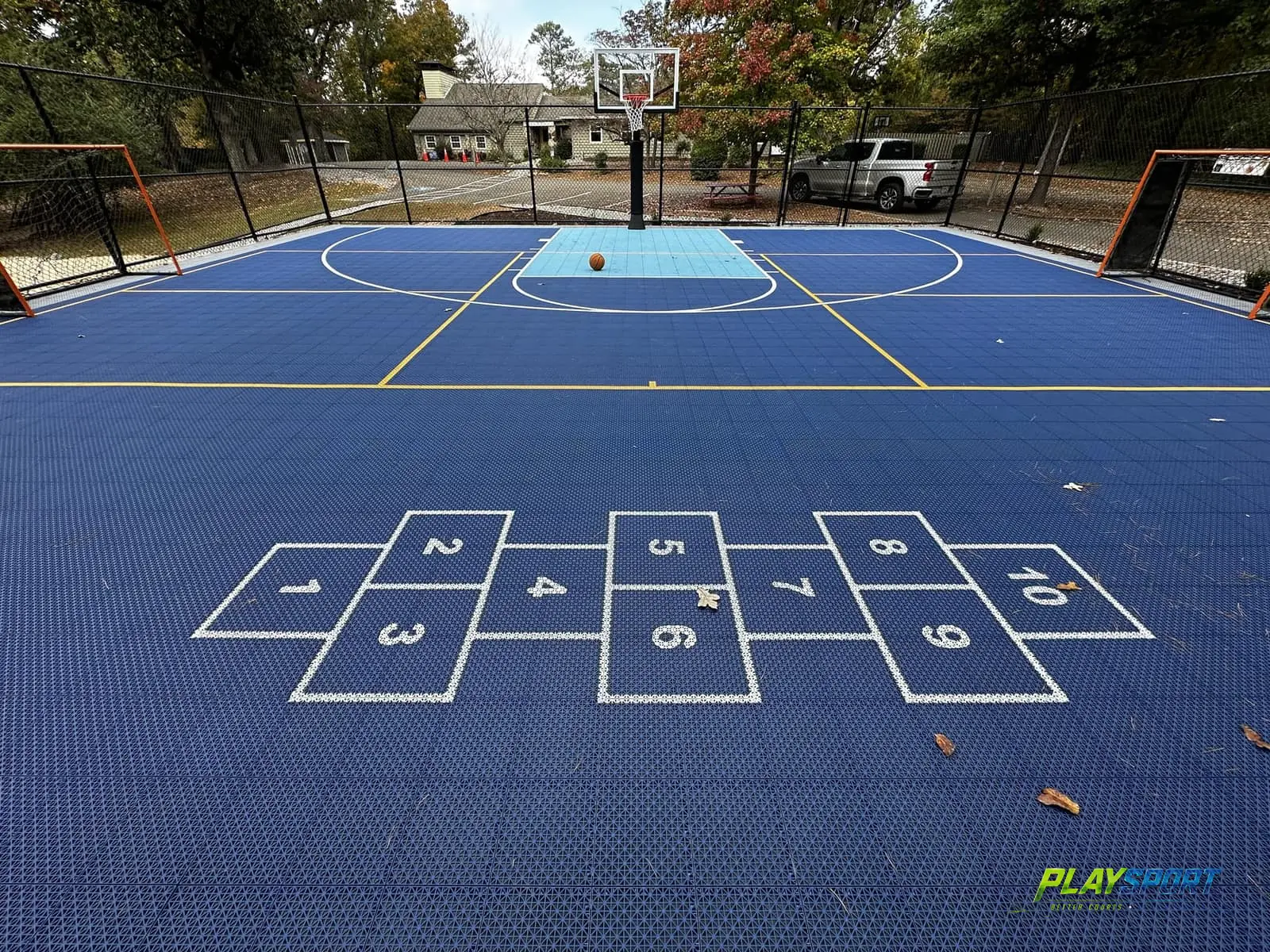 Blue family multi-sport court with a basketball hoop, hockey goals and hopscotch markings