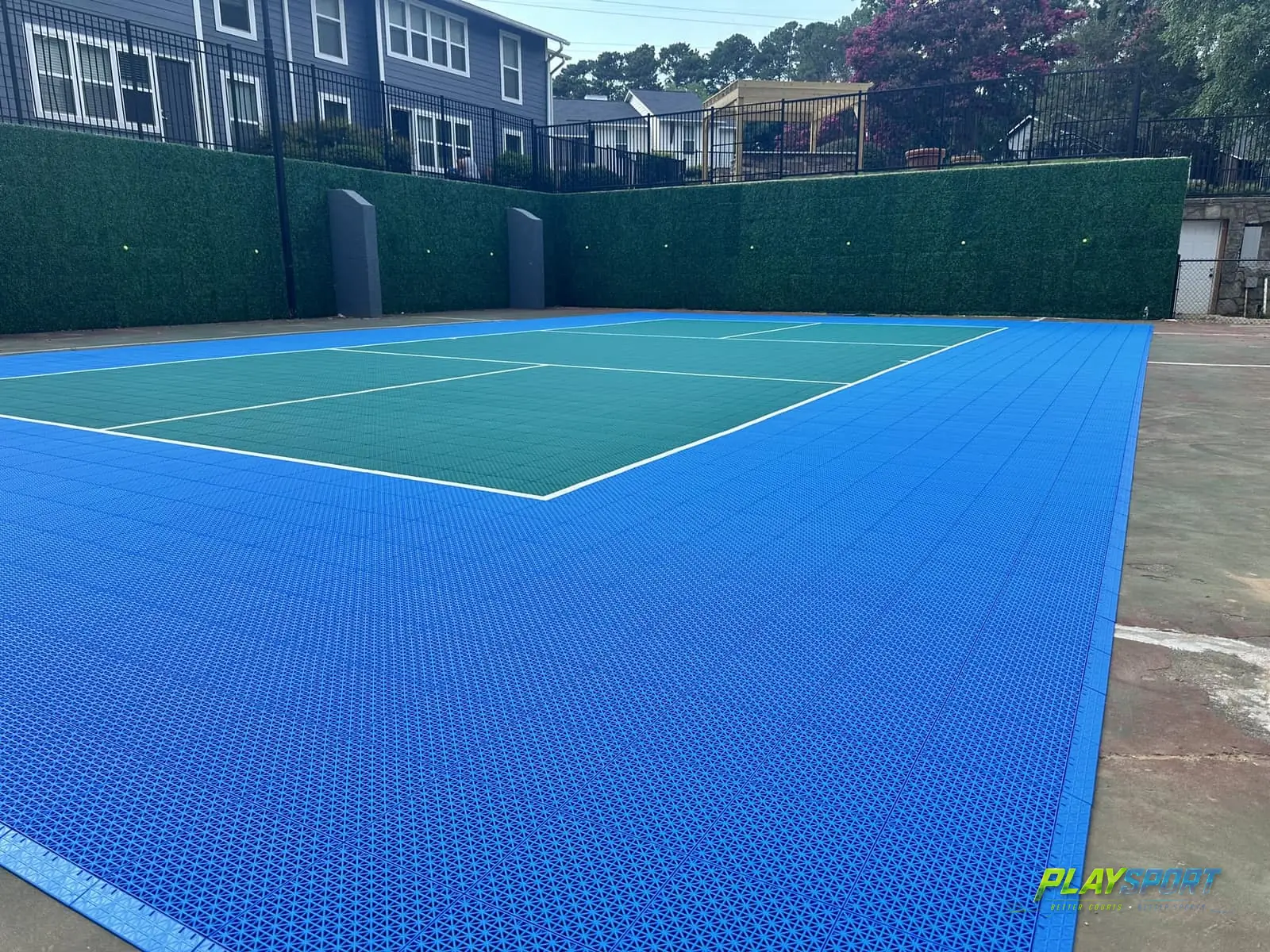 Bright blue and teal modular pickleball court with hedge privacy walls