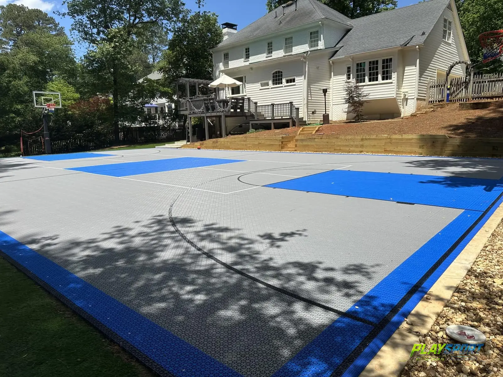 Grey and blue PlaySport CORE tile basketball court below a terraced backyard
