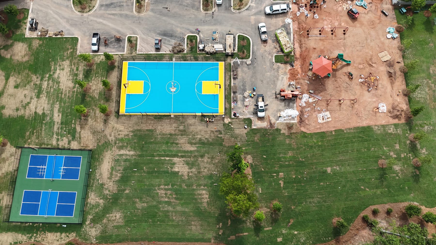 Aerial view of the finished project — blue and yellow PlaySport basketball court and two new pickleball courts installed on the cured concrete base