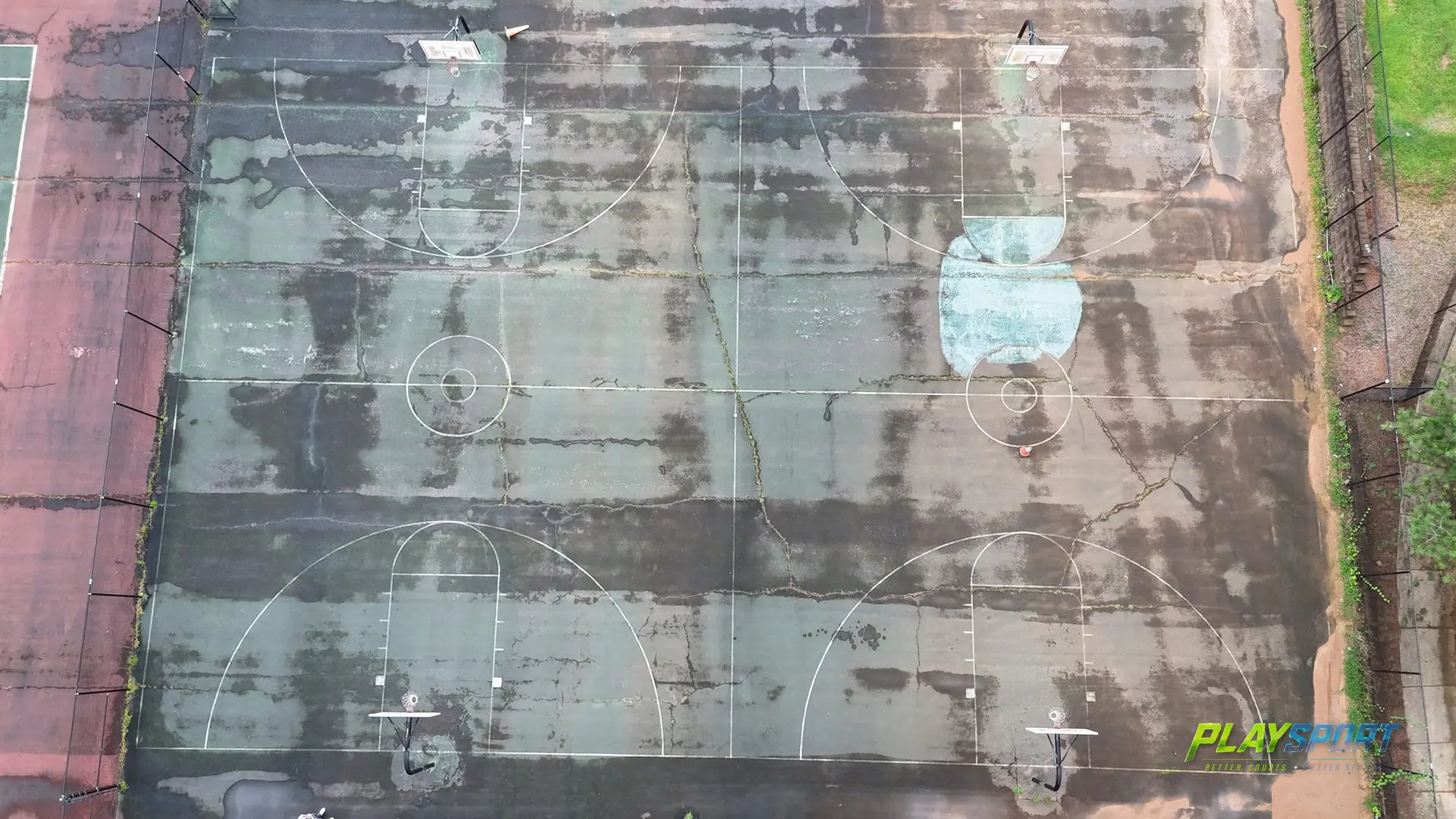 Cracked, faded painted-acrylic basketball court with weeds in the seams, the kind of surface PlaySport tiles replace