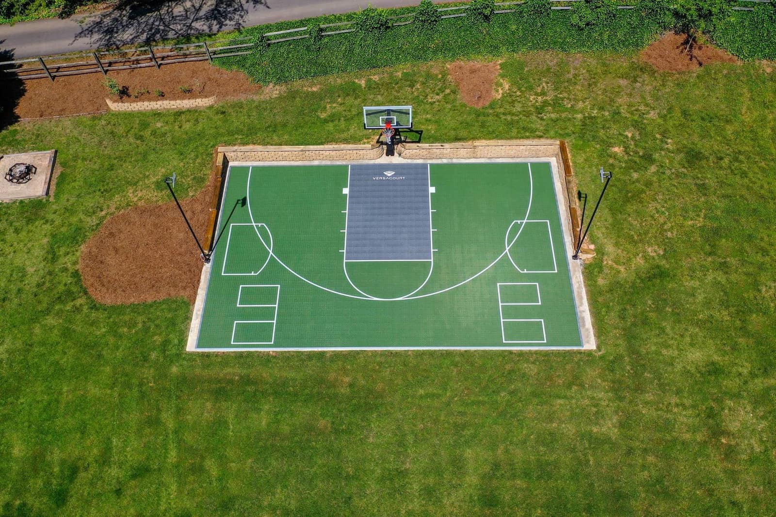 Aerial view — green multi-sport court with grey hockey lane and retaining wall