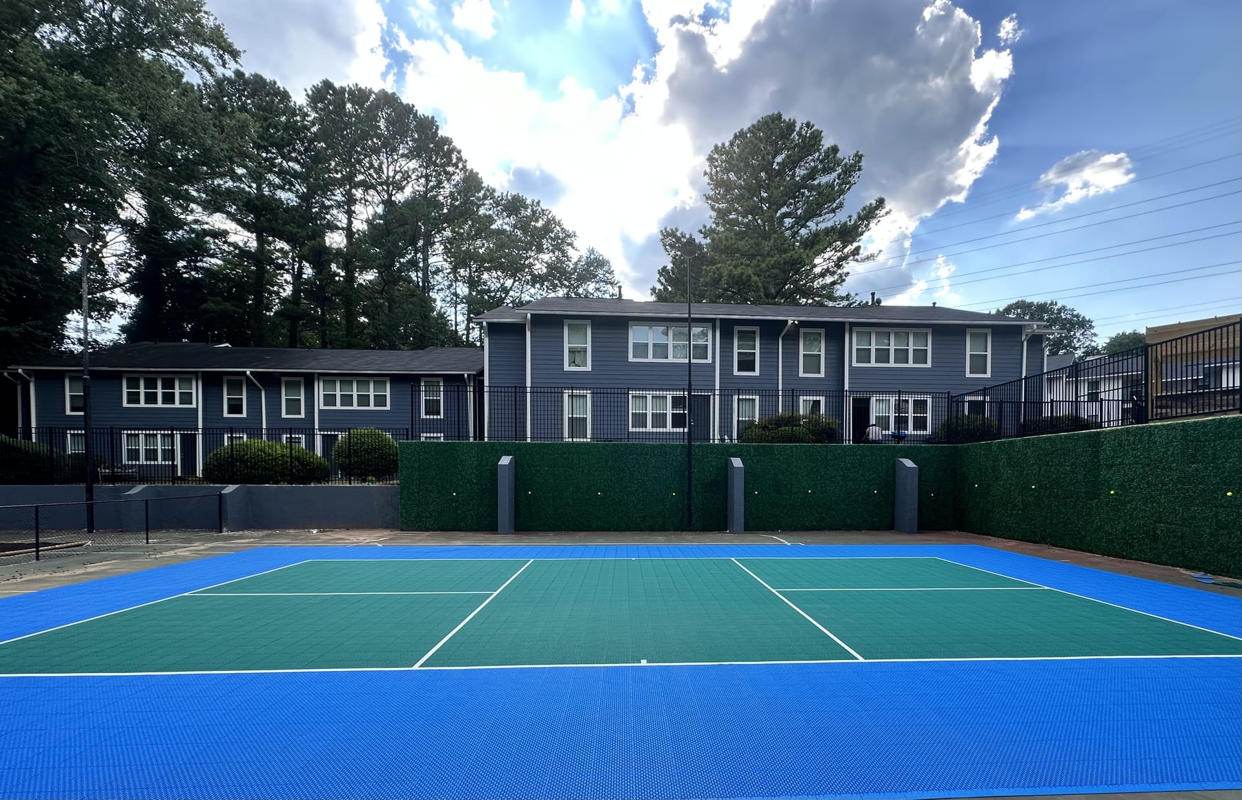 Blue and teal pickleball court at a townhome community with hedge privacy wall