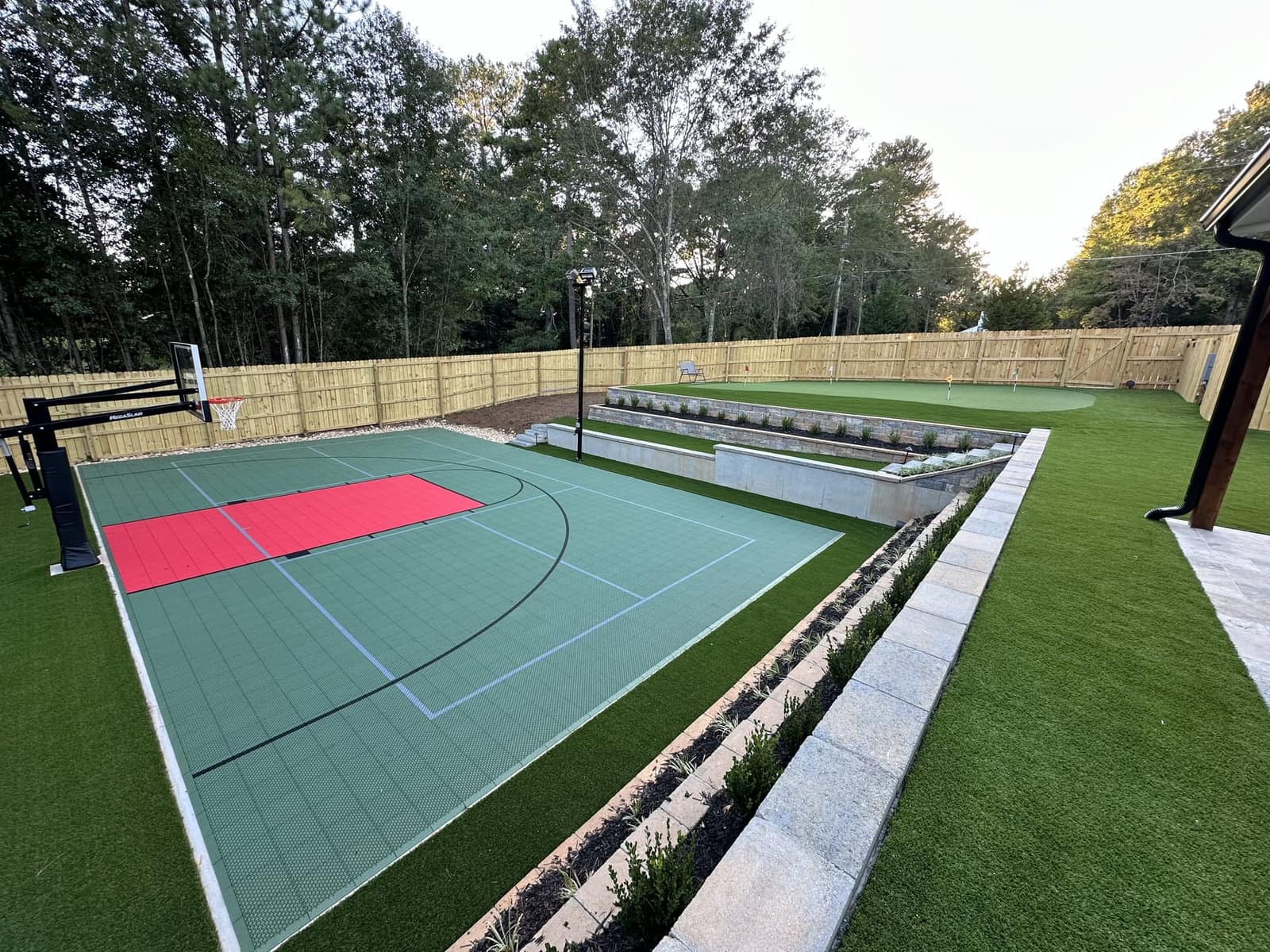 Sage green half court with red key beside a putting green and turf lawn