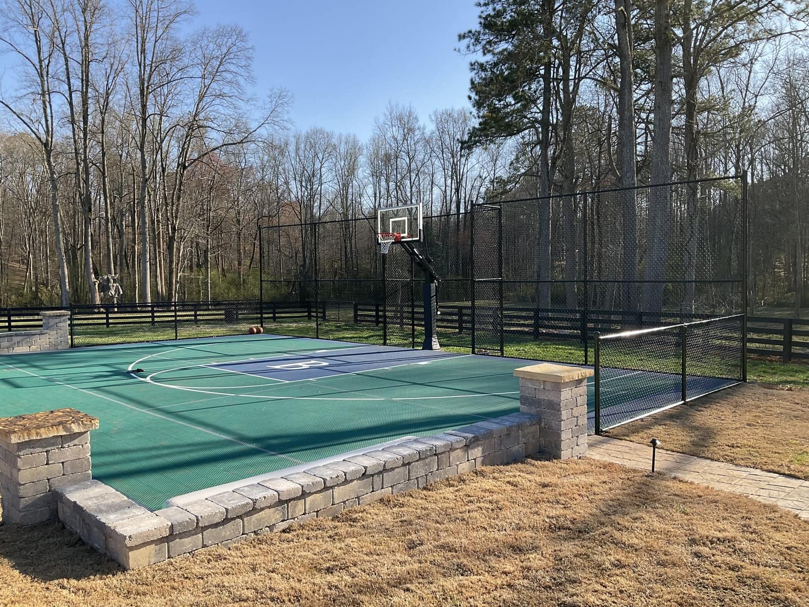 Green backyard basketball court with stone knee walls and black fence enclosure
