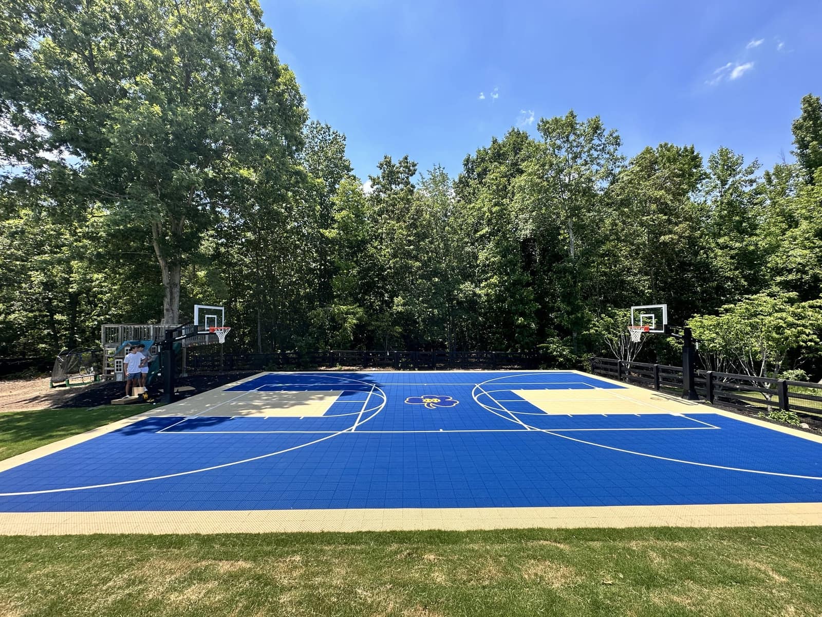 Full-size royal blue backyard basketball court with custom center logo and two hoops