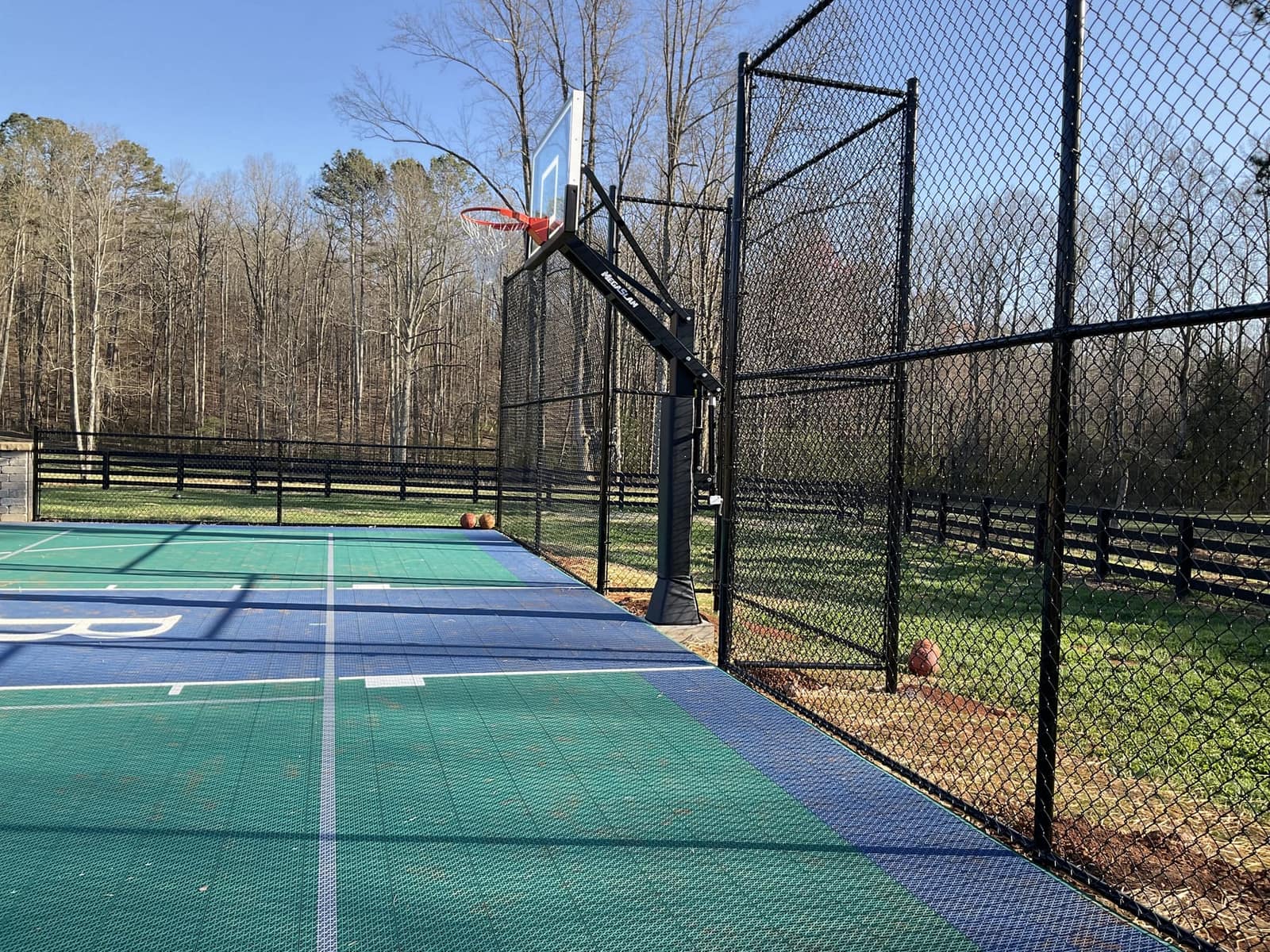 Green and blue backyard court corner with black chain-link fence enclosure