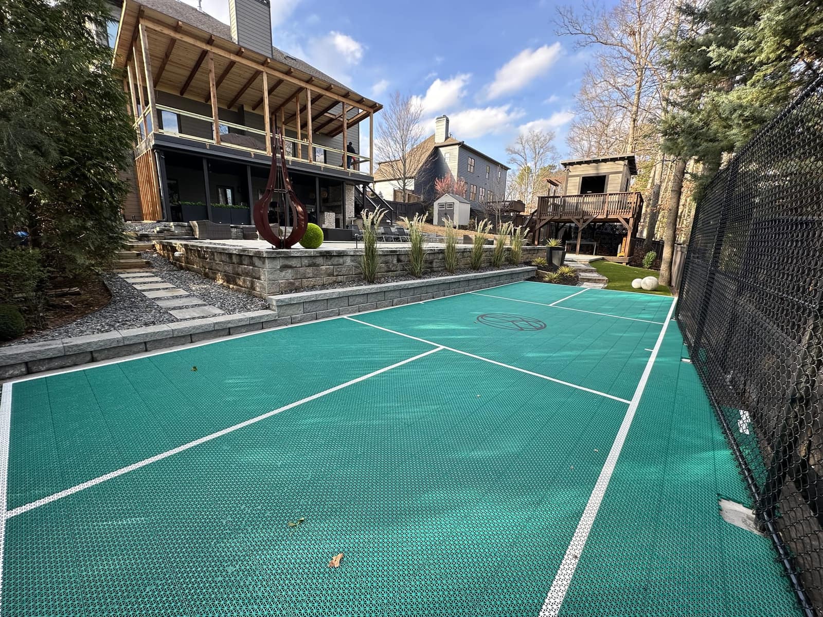 Teal pickleball court custom-fit into a terraced backyard below a modern deck