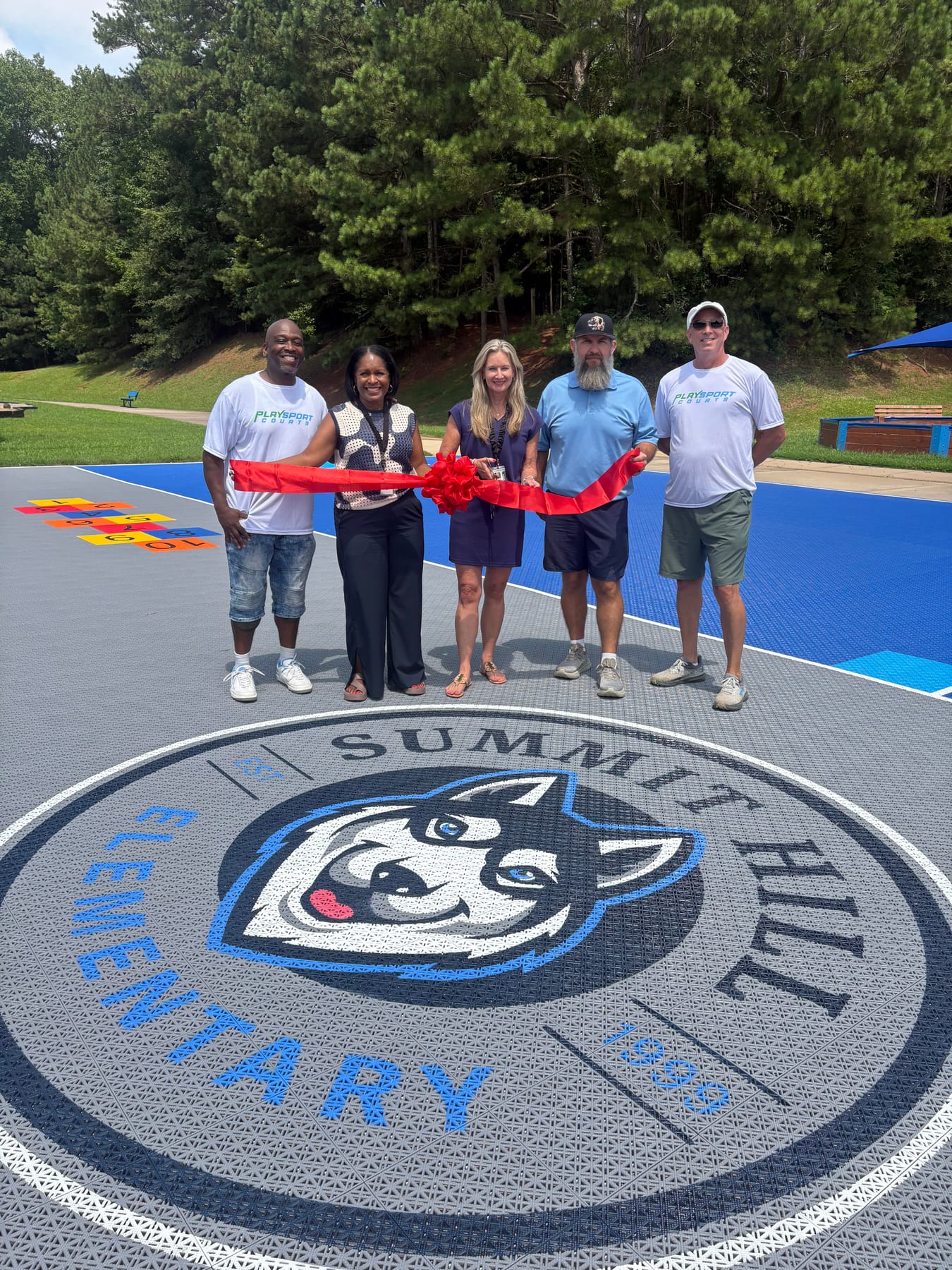 Ribbon cutting ceremony at Summit Hill Elementary's new PlaySport multi-sport court, standing on the custom Husky logo at center court