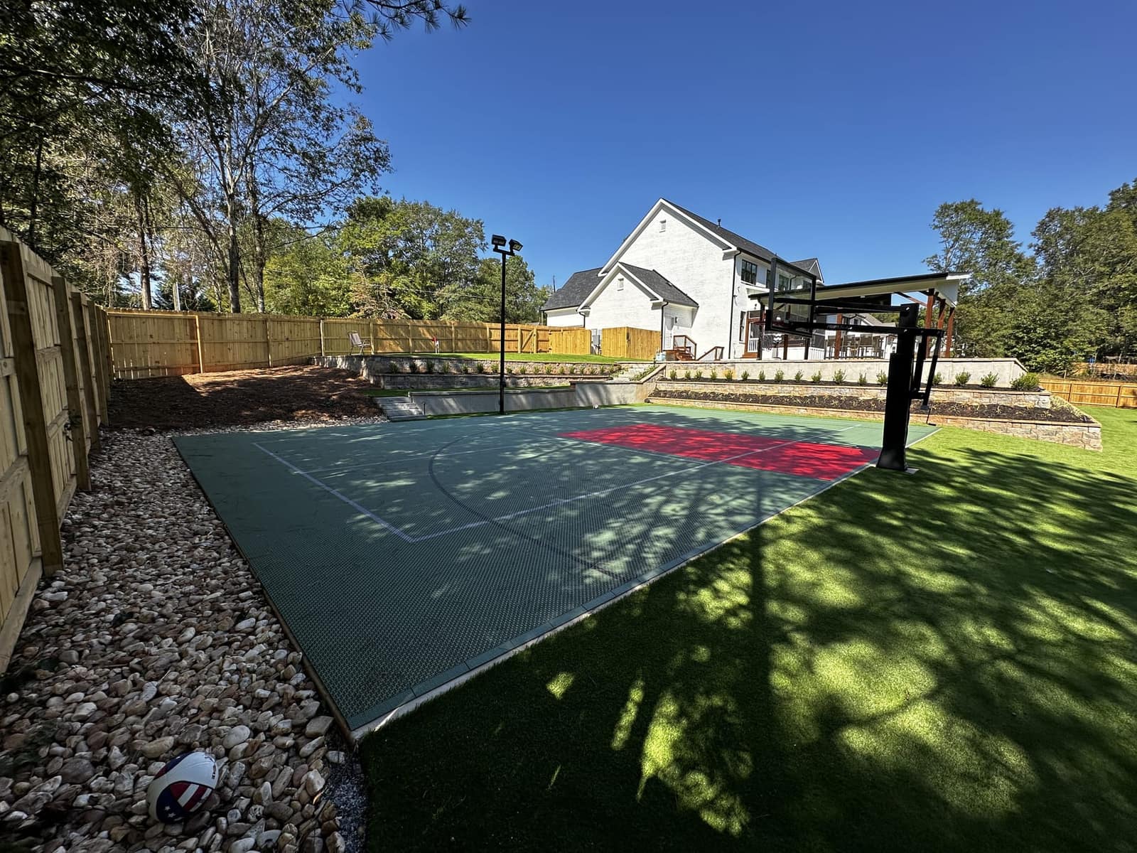 Sage green court with red key surrounded by fresh turf and river-rock border