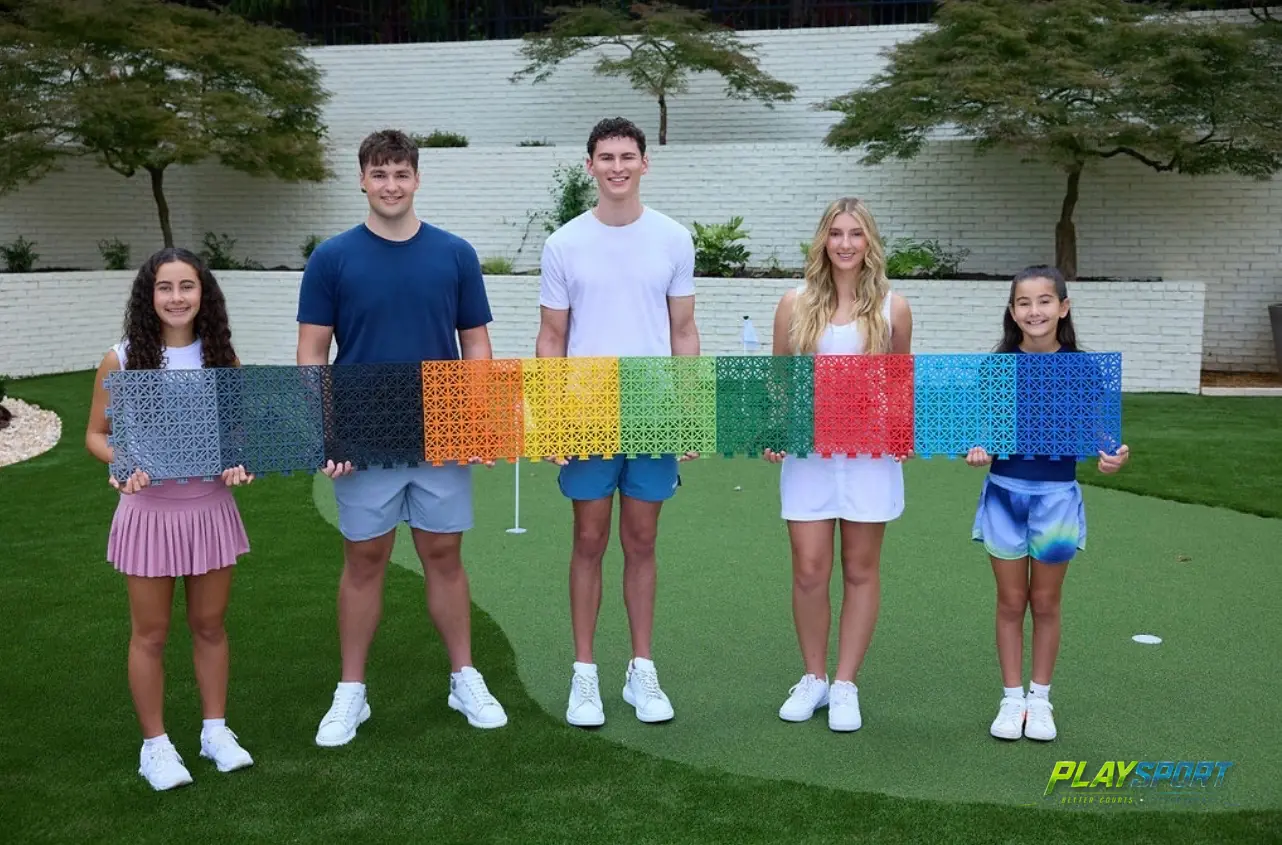 PlaySport Courts team holding the full range of modular sports court tile colors on a backyard putting green