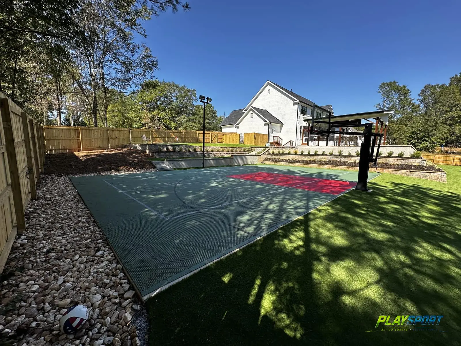 Sage green modular basketball court with a red key surrounded by fresh turf and a river-rock border