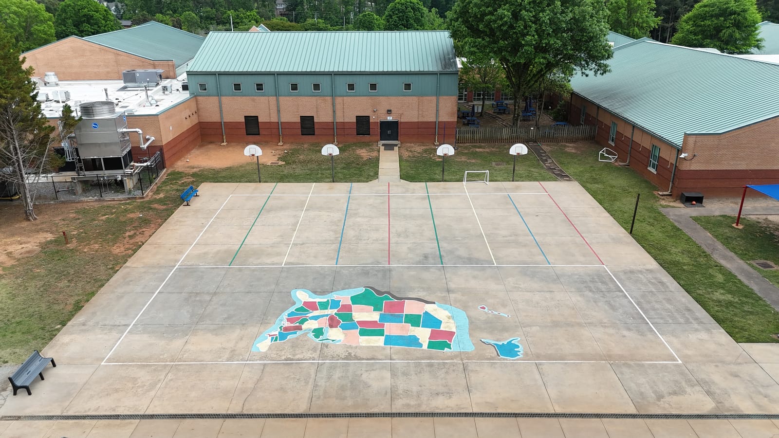 Aerial view of a faded school playground before resurfacing — worn painted lines and a peeling USA map on bare concrete at Summit Hill Elementary