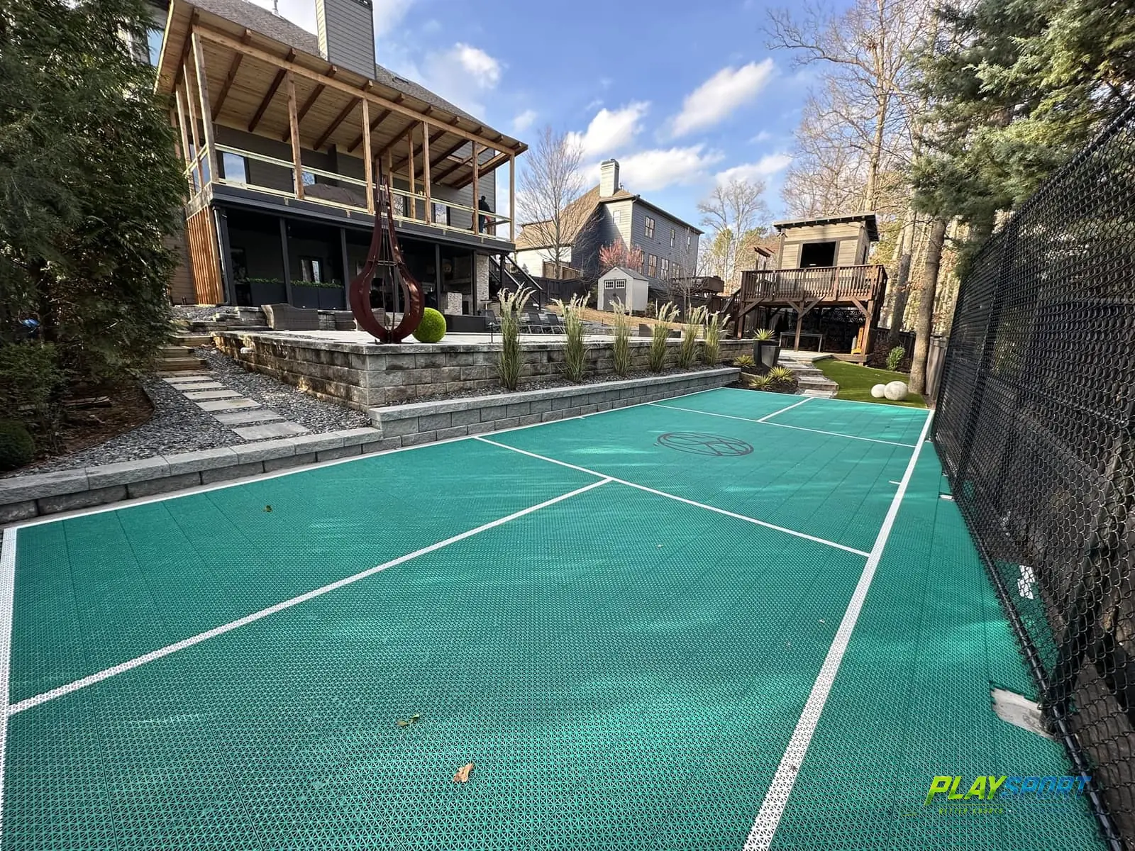 Teal modular pickleball court custom-fit into a terraced backyard below a modern deck