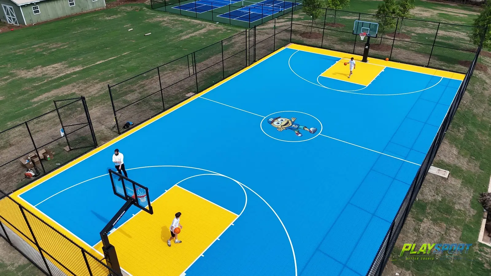 Blue and yellow PlaySport X Court basketball court with a custom center logo, corner drone view